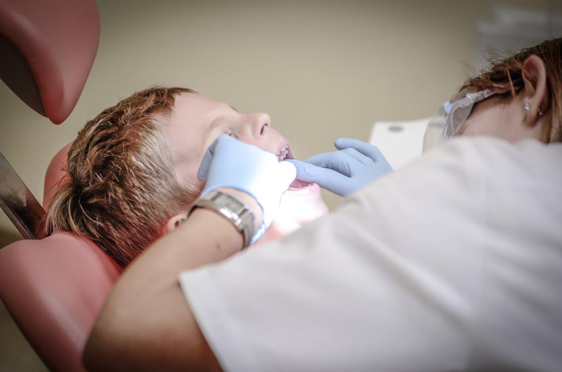 Free Dentist Woman Wearing White Gloves and White Scrubsuit Checking Boy's Teeth Stock Photo