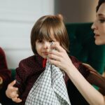 Free Woman assisting a child with a napkin during a meal indoors, highlighting care and family bonding. Stock Photo