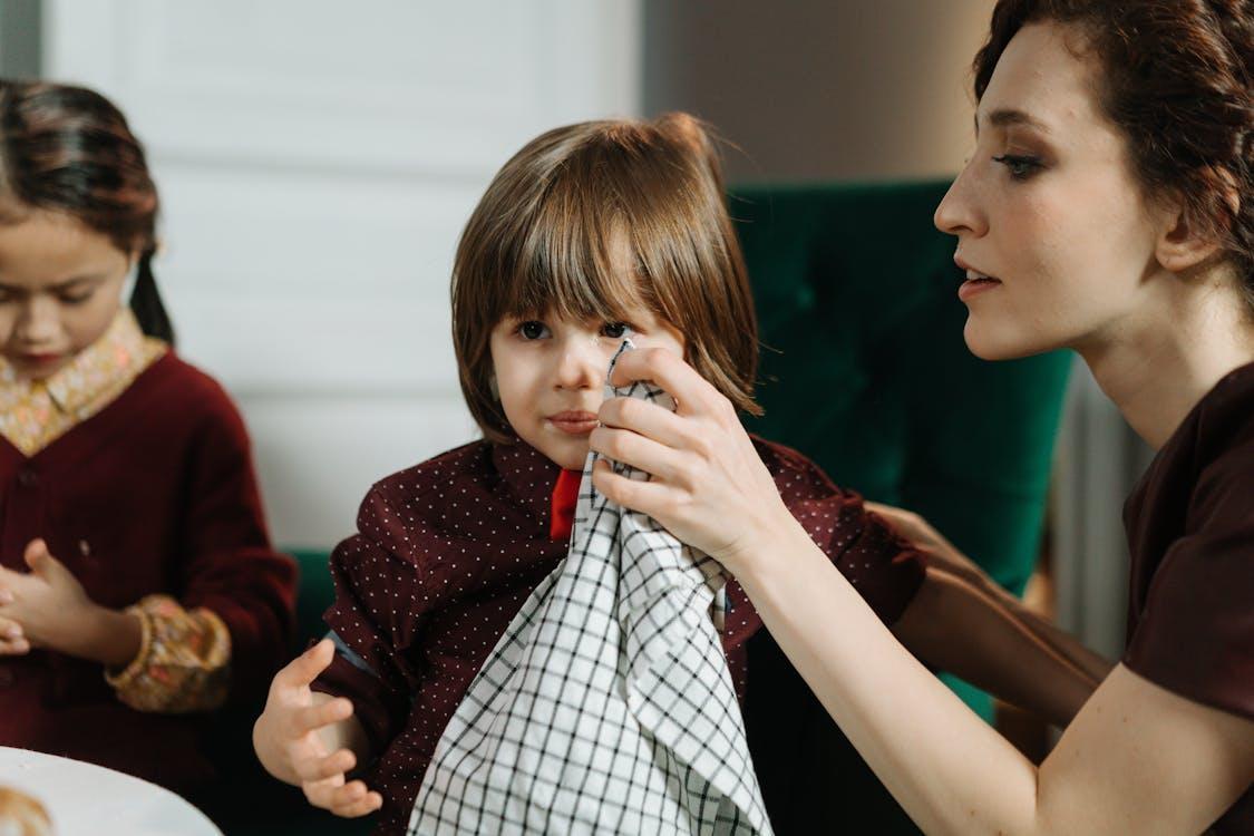 Free Woman assisting a child with a napkin during a meal indoors, highlighting care and family bonding. Stock Photo