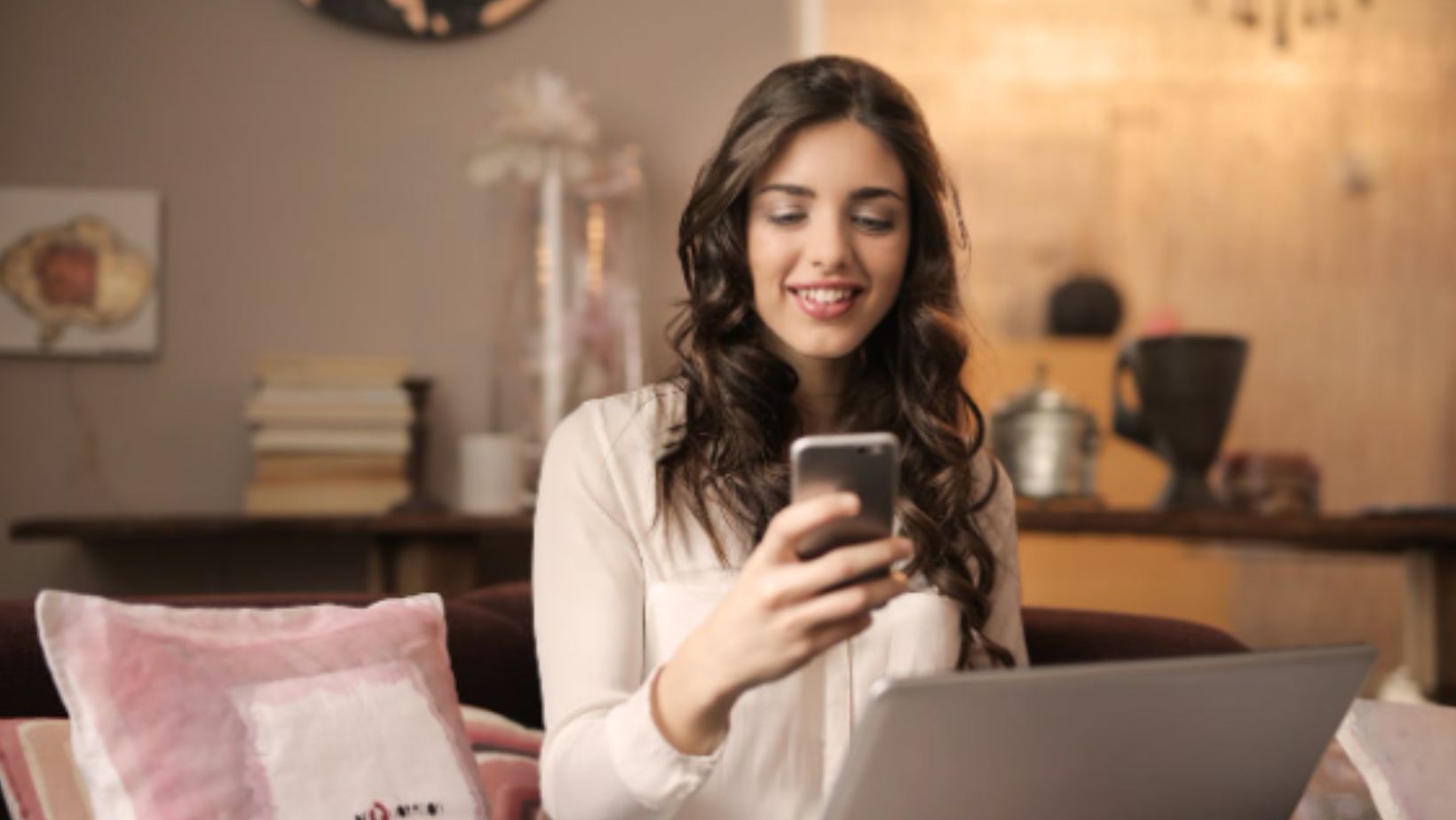 Woman Sitting on Sofa While Looking at Phone With Laptop on Lap