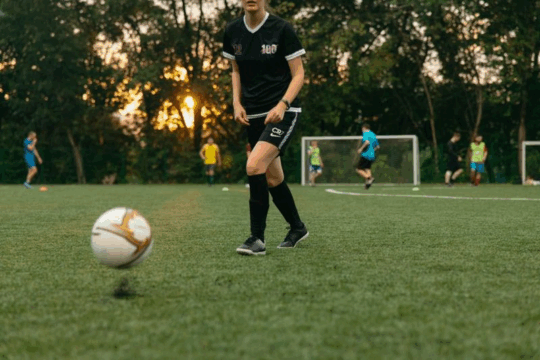Soccer player chases ball at sunset.