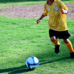 Youth soccer player dribbling blue ball.